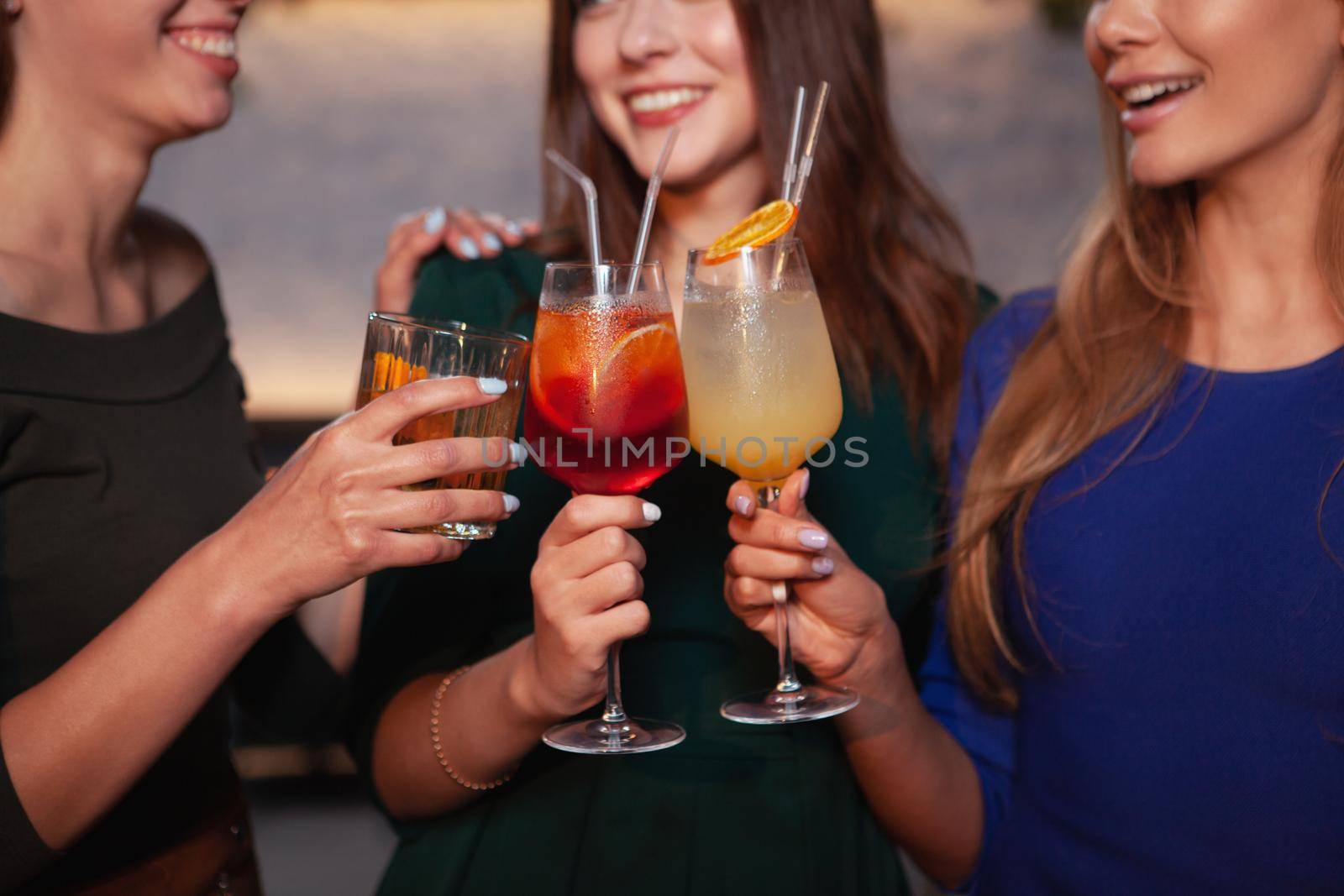 Cropped shot of happy female friends clinking cocktail glasses together, celebrating together