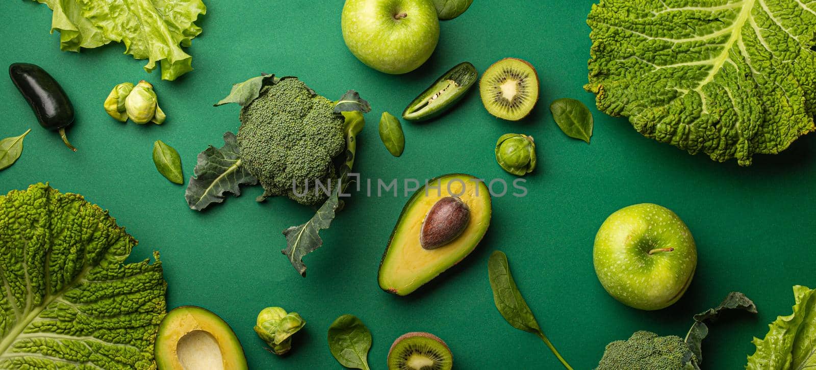 Creative layout healthy organic food concept made of green fruit and vegetables on green background flat lay: avocado, kale, broccoli, Brussels sprouts, kiwi, peppers, apple, cabbage top view.