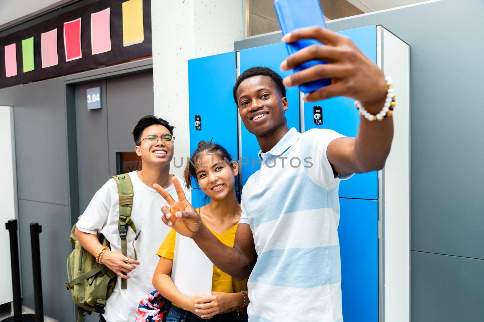 Happy group of teen multiracial classmate take a selfie in high school corridor next to lockers. Friendship concept. Back to school concept.