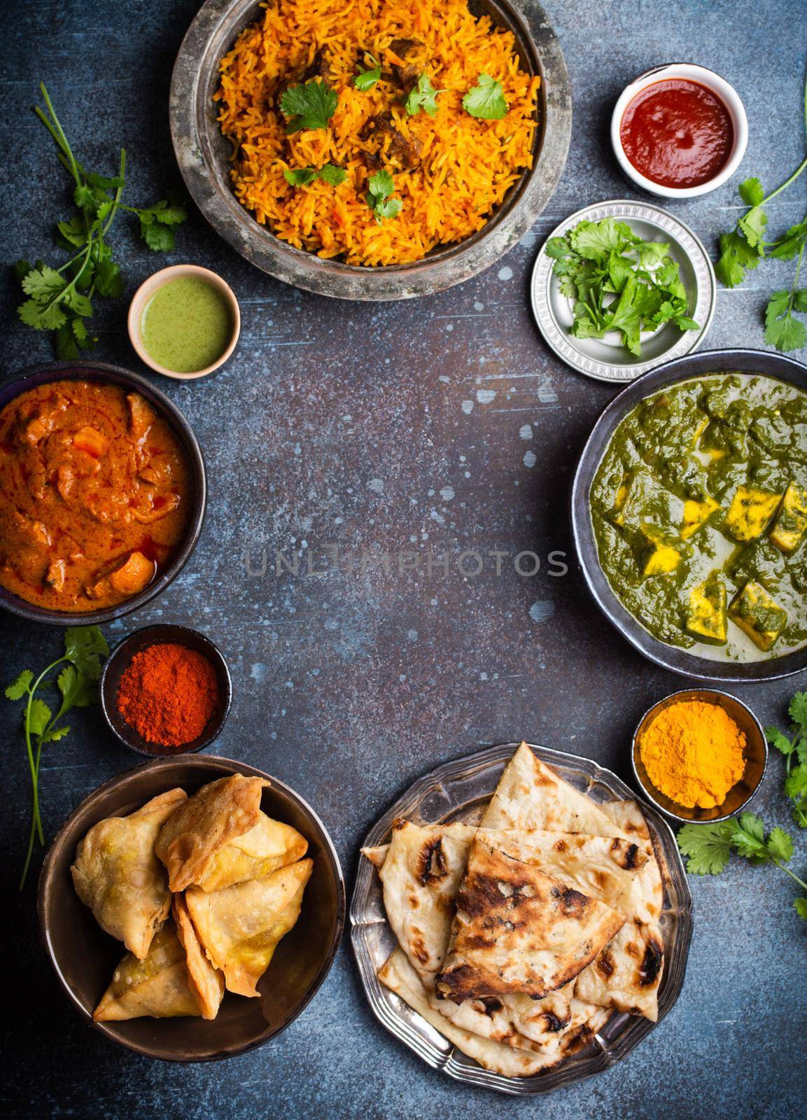 Overhead of Indian traditional dishes and appetizers: chicken curry, pilaf, naan bread, samosas, paneer, chutney on rustic background. Table with choice of food of Indian cuisine, space for text