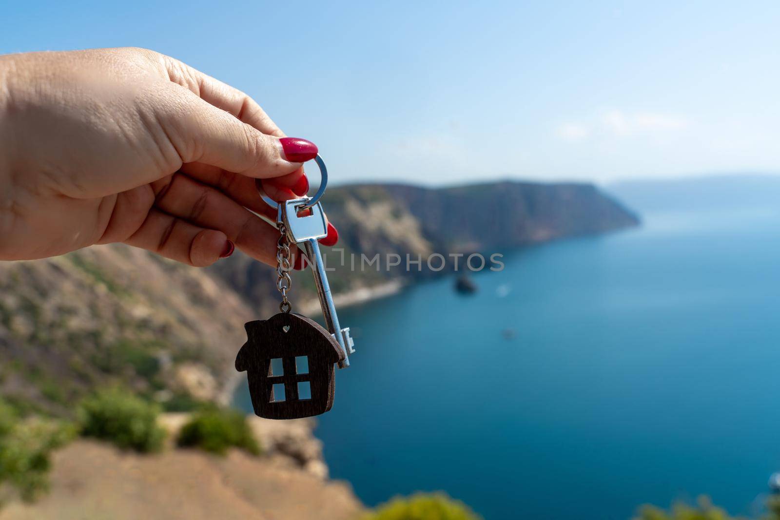 Keys with a keychain in the shape of a house in a female hand against the backdrop of the sea. The concept of buying a house, apartment, real estate, young family, mortgage loan, rental housing