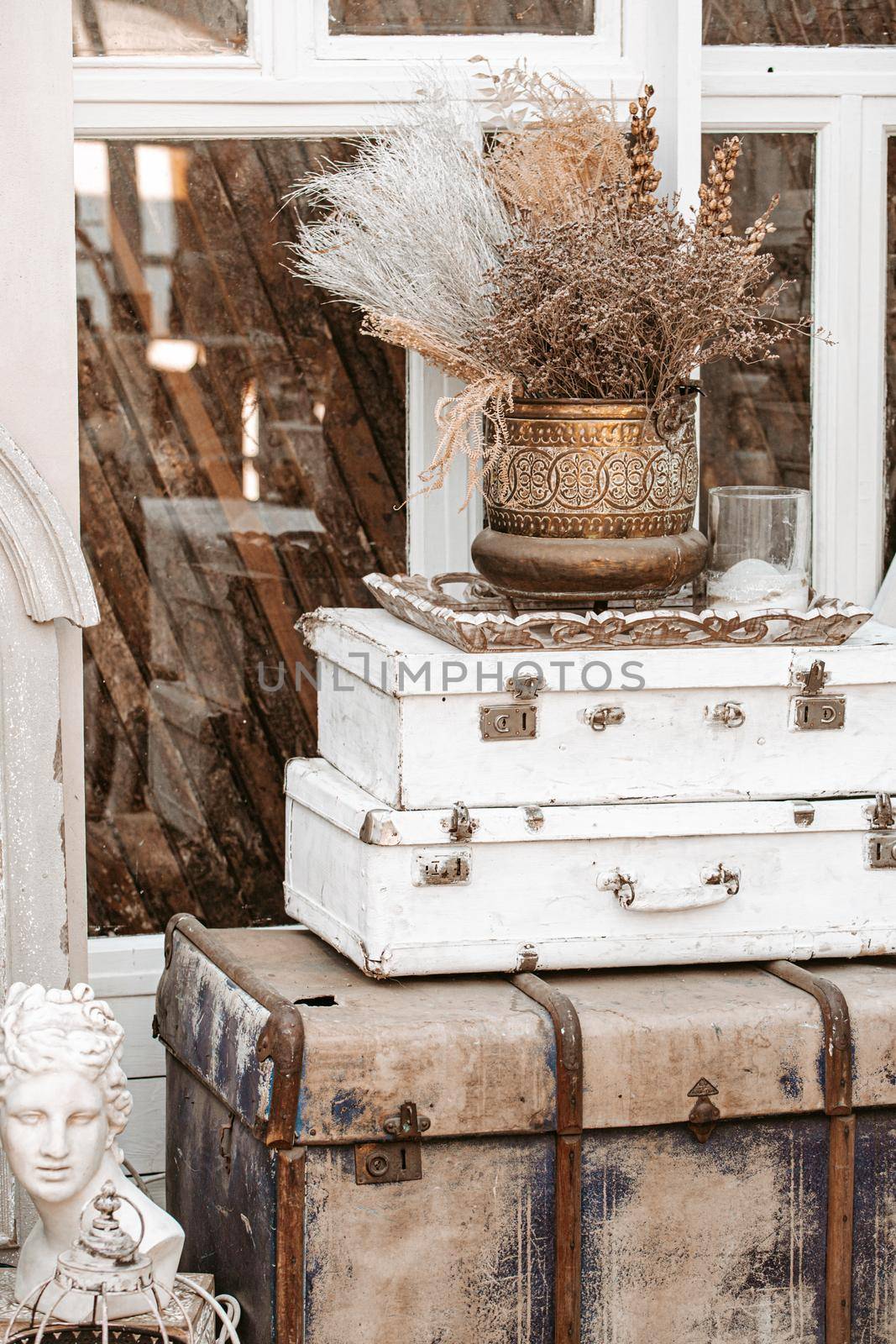 Pile of vintage ancient suitcases trunks in form of tower with old vase on top next to window in shabby chic interior room in Provence french cottage country style, retro luggage of traveler