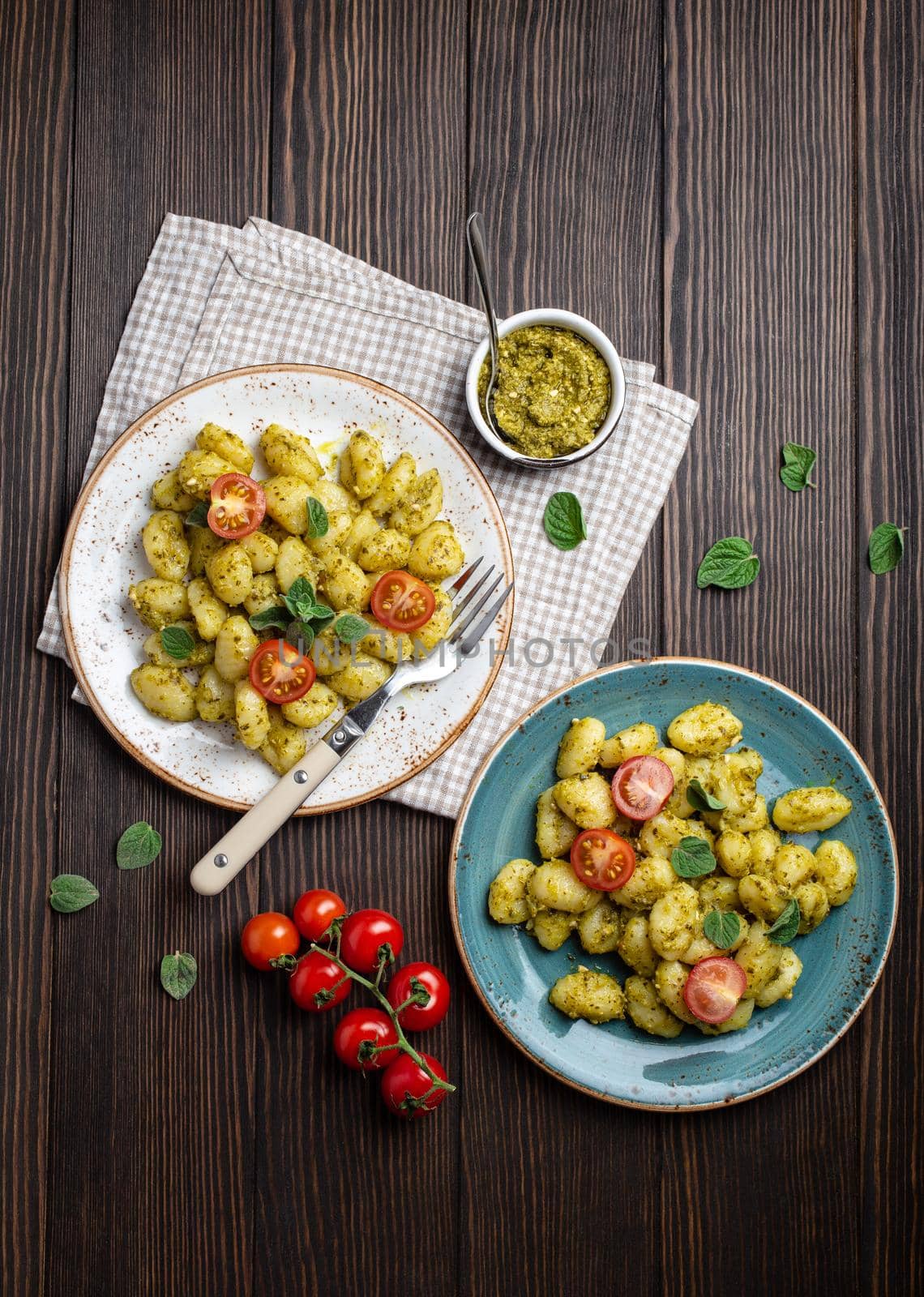 Gnocchi in plates with green pesto sauce, tomatoes and herbs on rustic wooden background, close up, top view. Traditional dish of Italian cuisine