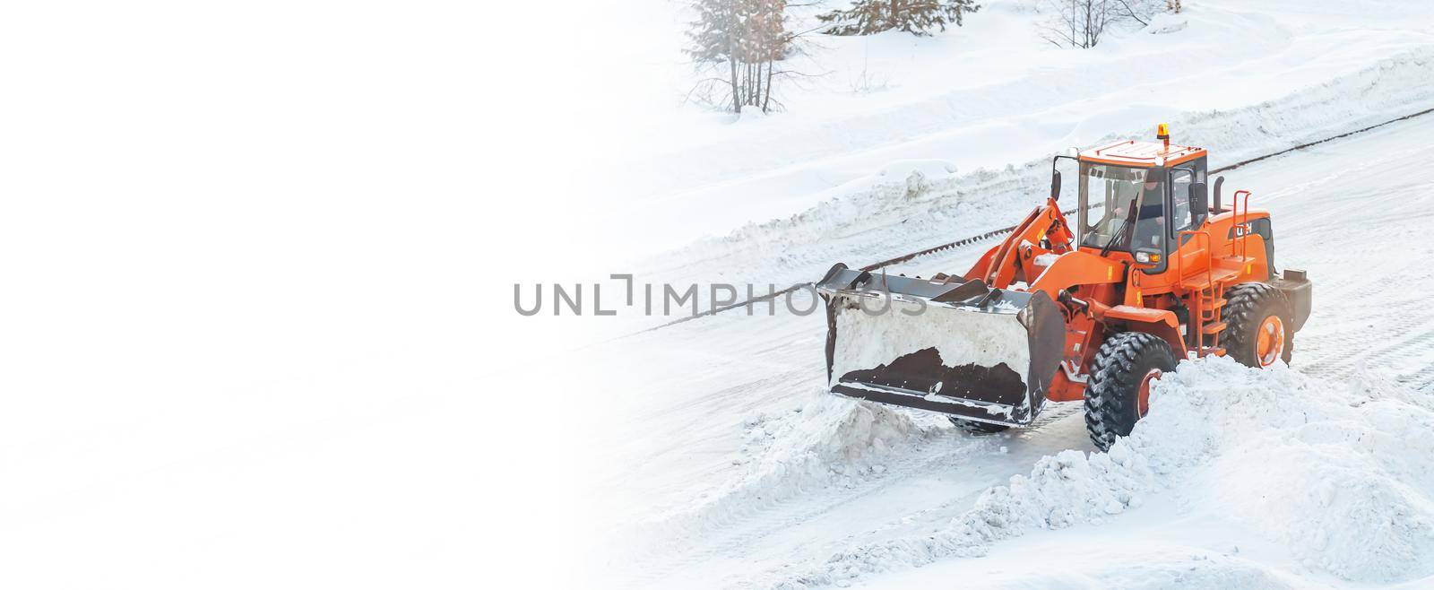 A large orange tractor removes snow from the road and clears the sidewalk. Cleaning and clearing roads in the city from snow in winter. Snow removal after snowfalls and blizzards. banner