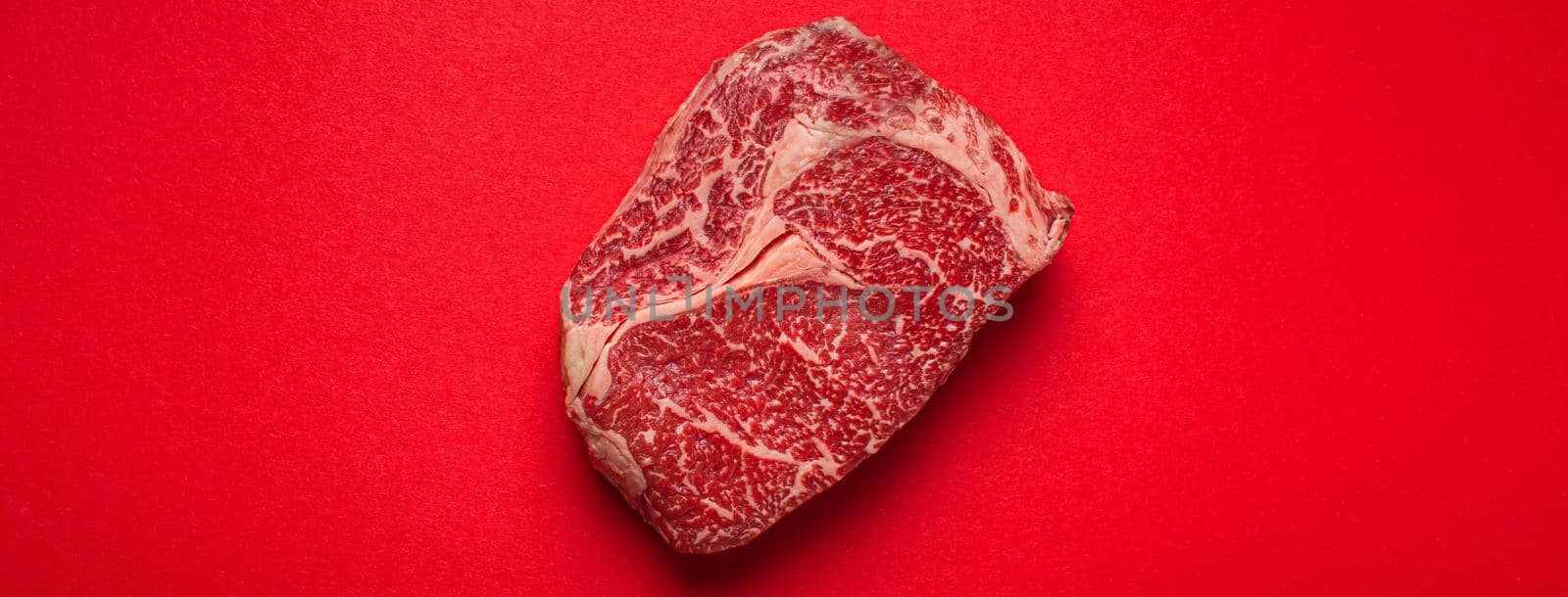 Raw fresh uncooked meat beef prime cut steak Ribeye on clean red background from above, beefsteak concept banner minimalism