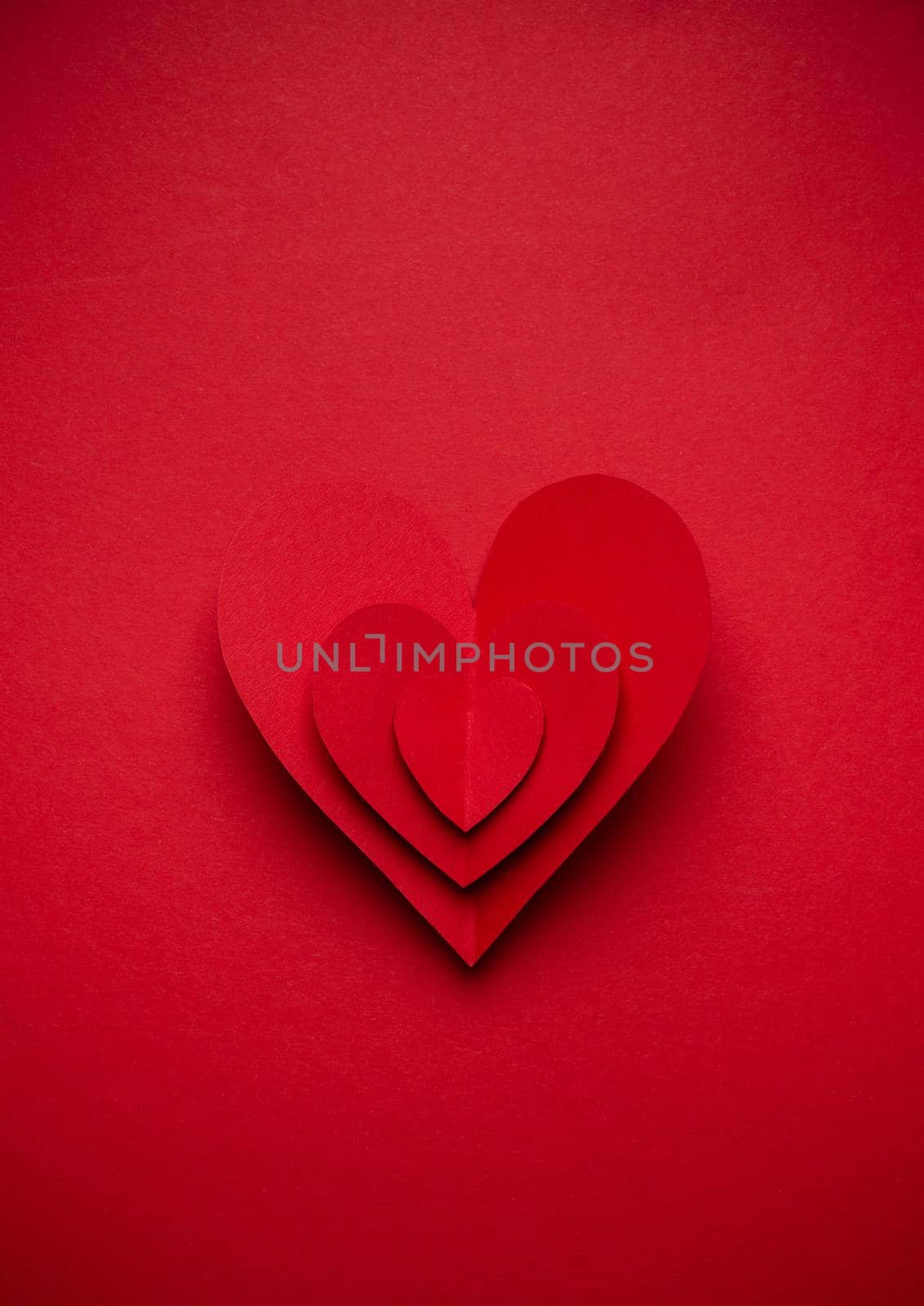 Big voluminous red heart cut from paper on red monochrome background, paper craft origami style, from above. Romantic Valentine's day symbol, love concept. Paper art design, 14 February celebration.