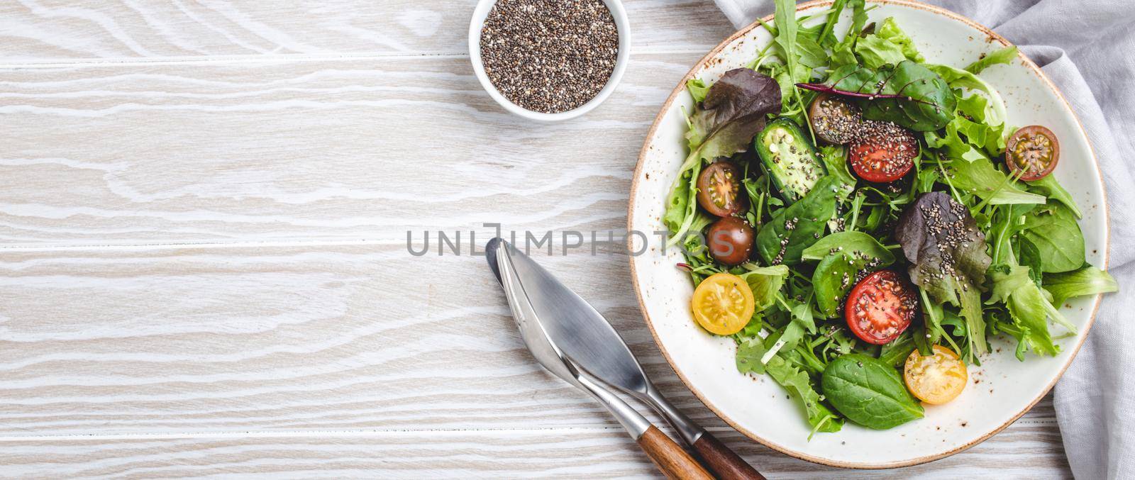 Vegetables vegetarian healthy salad with red yellow cherry tomatoes, green leafs and chia seeds on white plate on white wooden rustic background top view, healthy food and diet concept, space for text