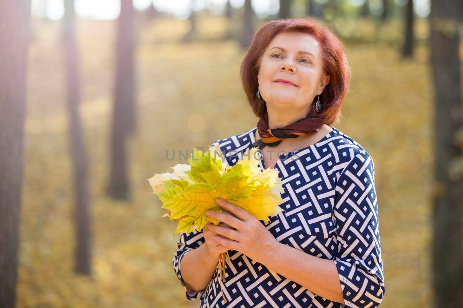 Fifty year old woman with a bouquet of autumn leaves in the park.Autumn age