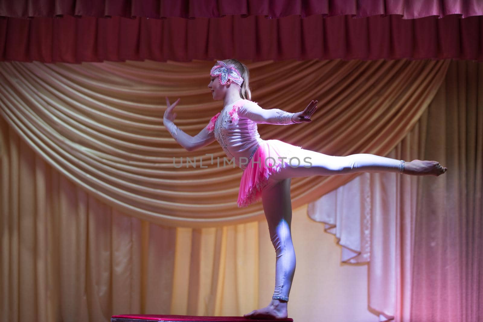 Beautiful girl acrobat gymnast performs on stage. by Sviatlana