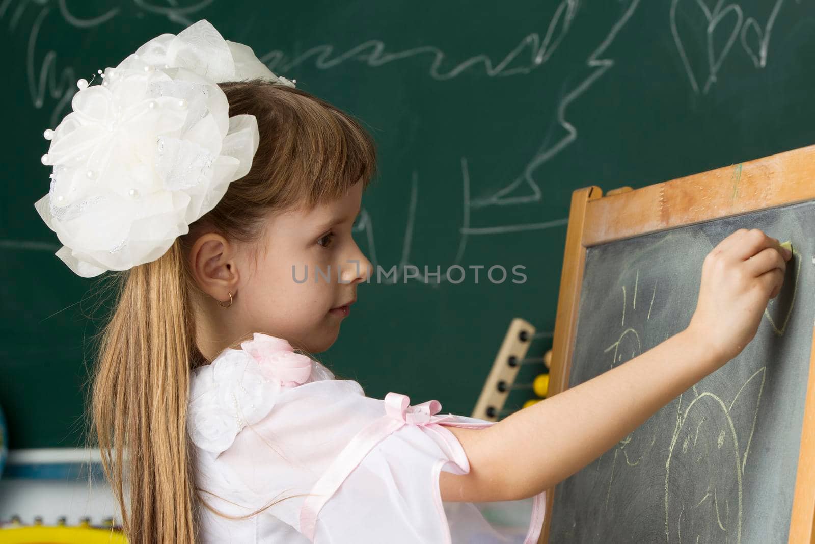 Schoolgirl of primary classes. Draw at the blackboard. Education at school. Girl with bows