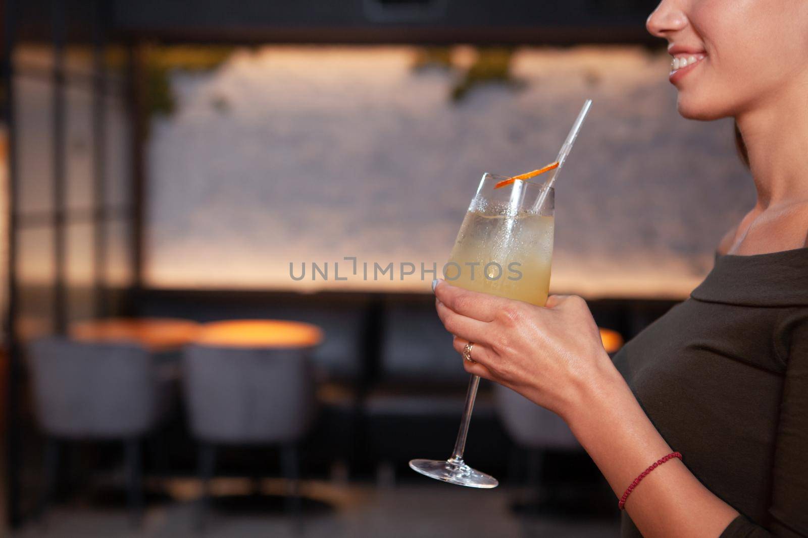 Cropped profile close up of a woman at the bar smiling, holding cocktail