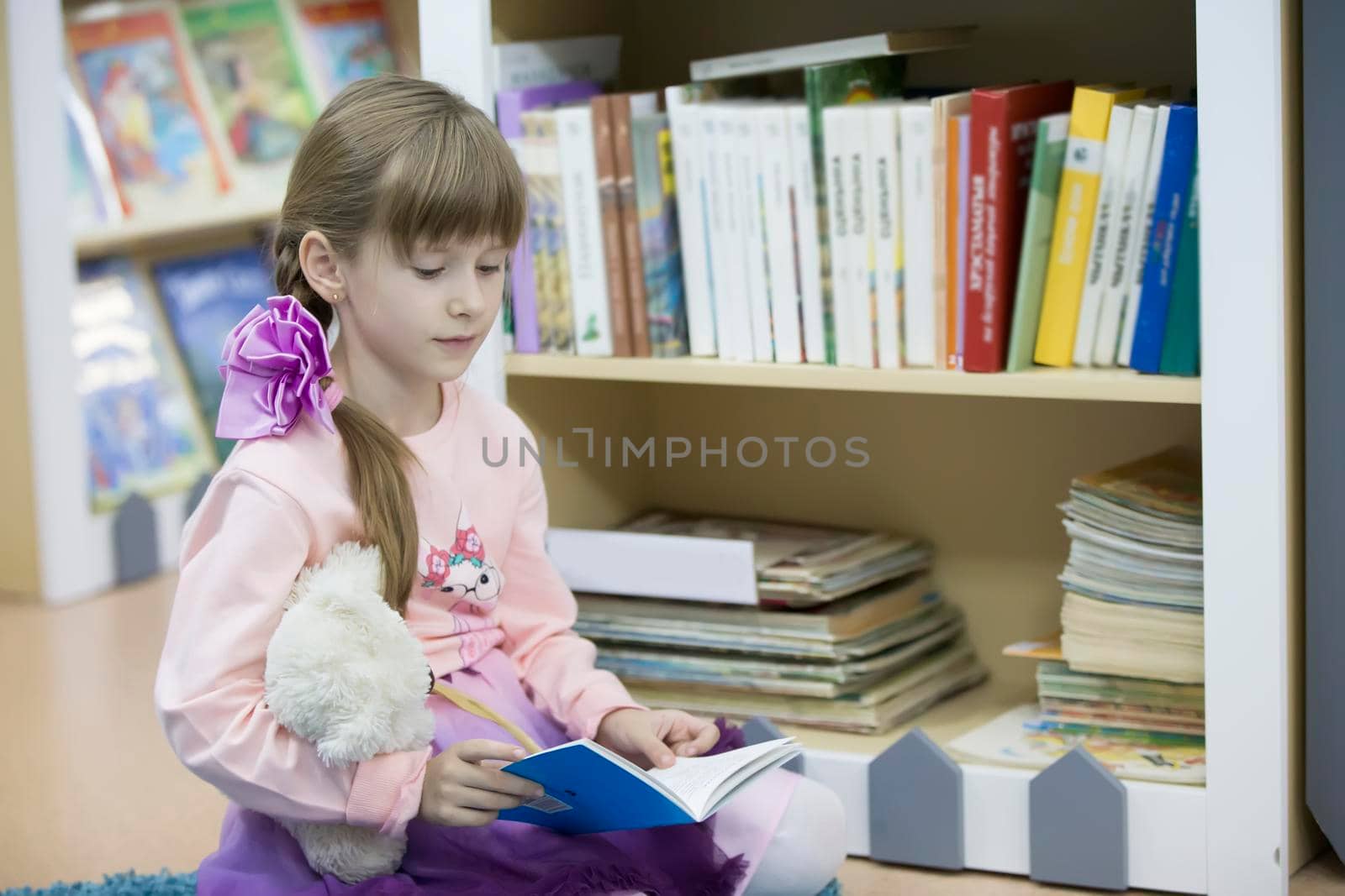 A preschool girl is reading a book. The child is in the library. Read books. by Sviatlana