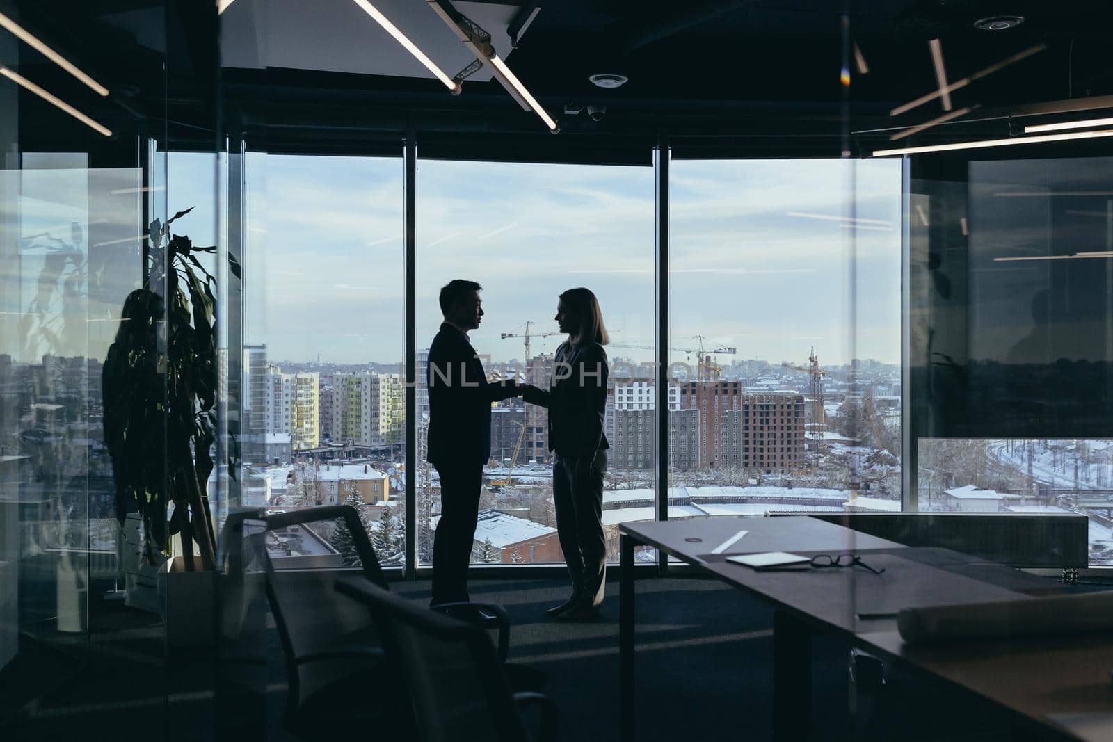 Silhouettes of two employees team of businessmen, Asian man and woman are consulting and communicating, working in a modern office by the window