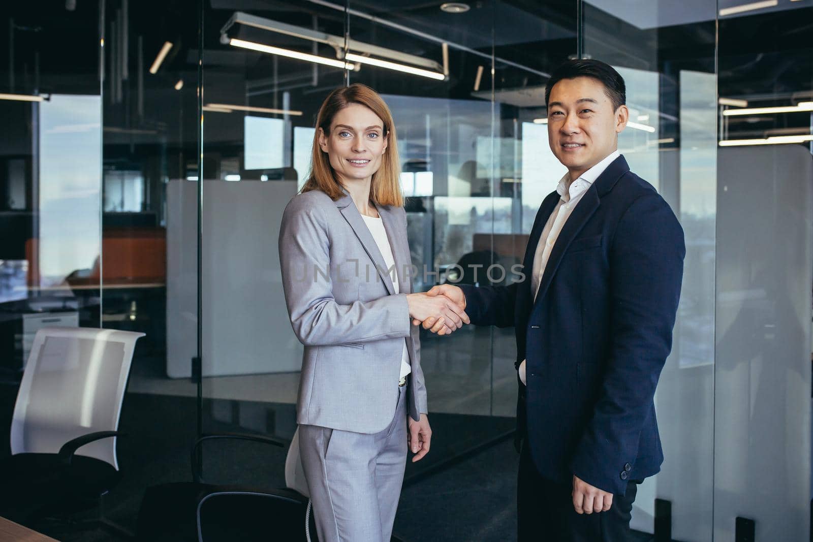 Asian businessman shakes hands with business woman employee, happy team of workers looking at camera and smiling, successful conclusion of negotiations