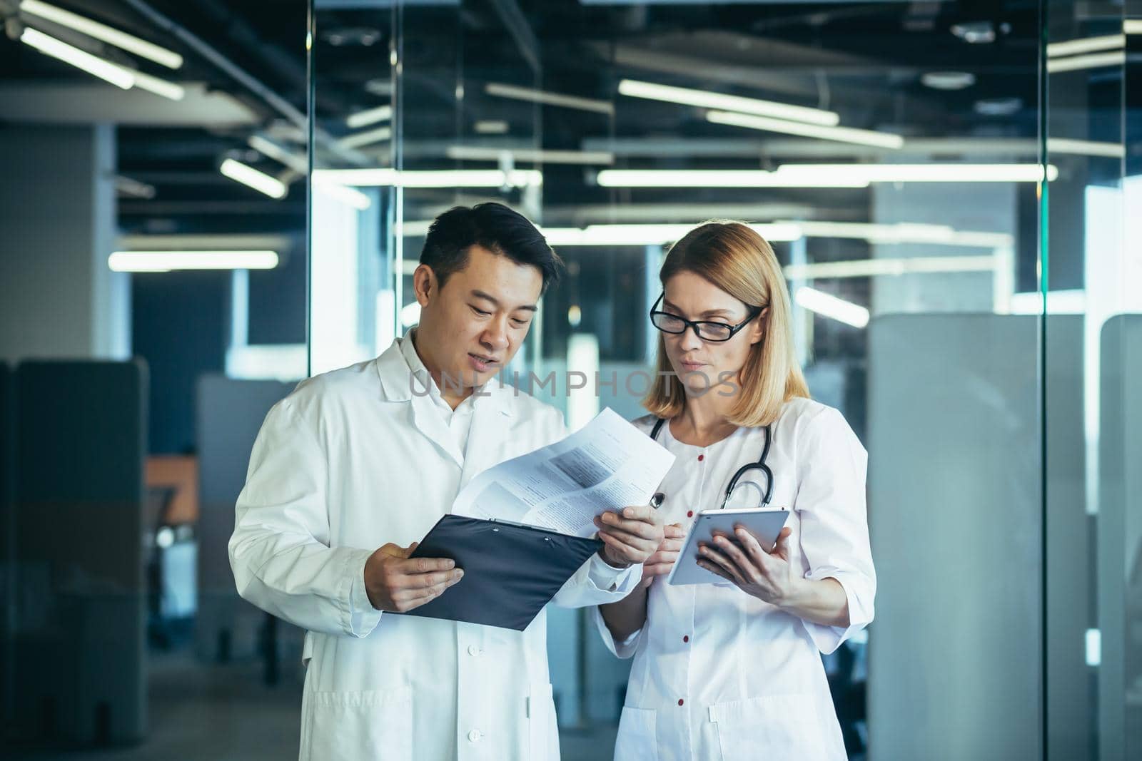 Two doctors, mixed race Asian man and Caucasian woman, communicate, discuss patient treatment, work in a modern clinic