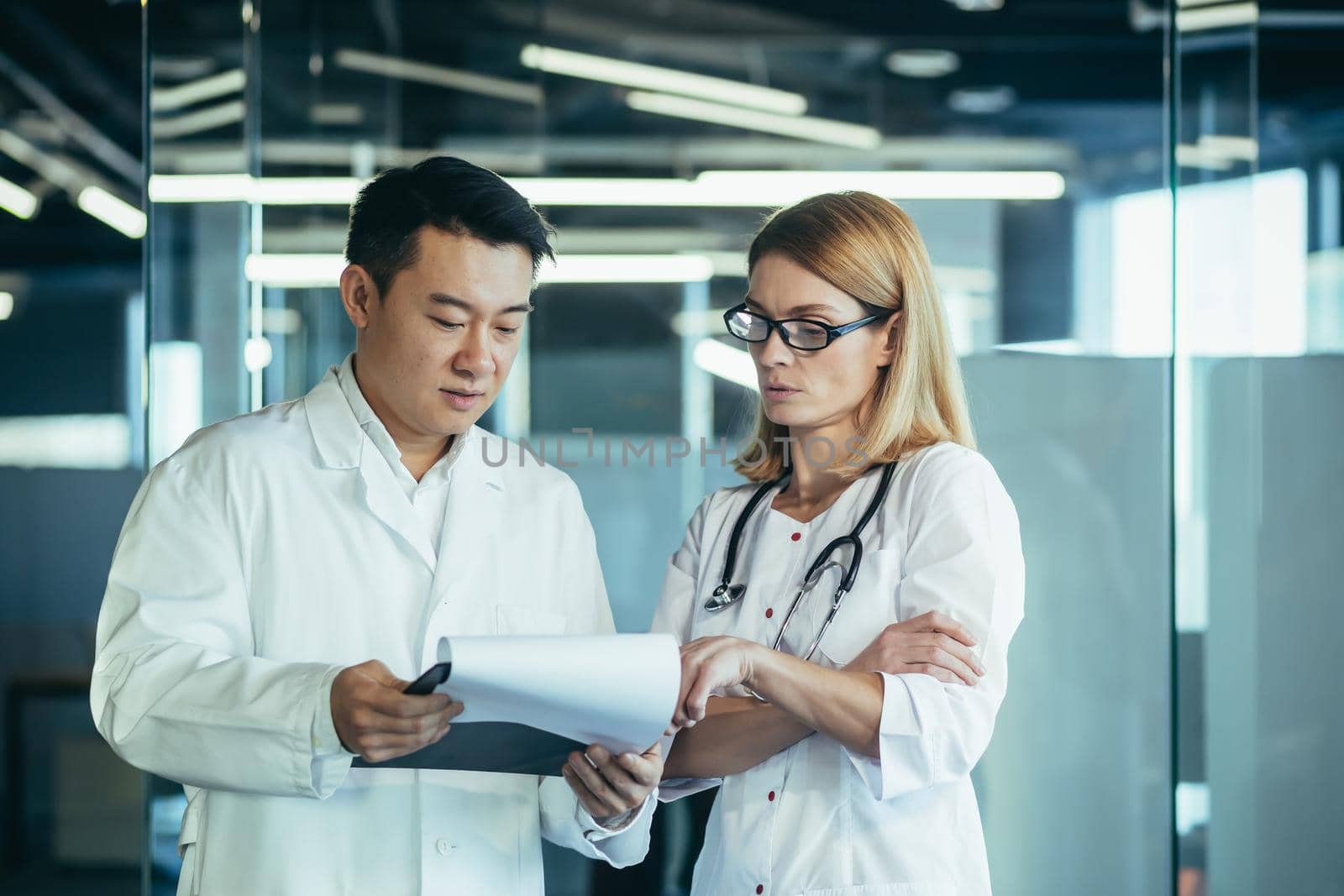 Two doctors, mixed race Asian man and Caucasian woman, communicate, discuss patient treatment, work in a modern clinic