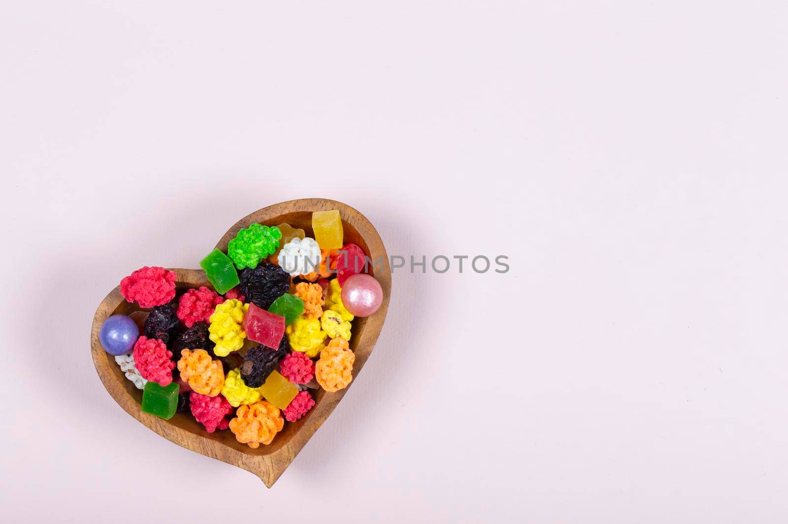 Colorful sweets and candies are poured into a heart-shaped wooden vase.