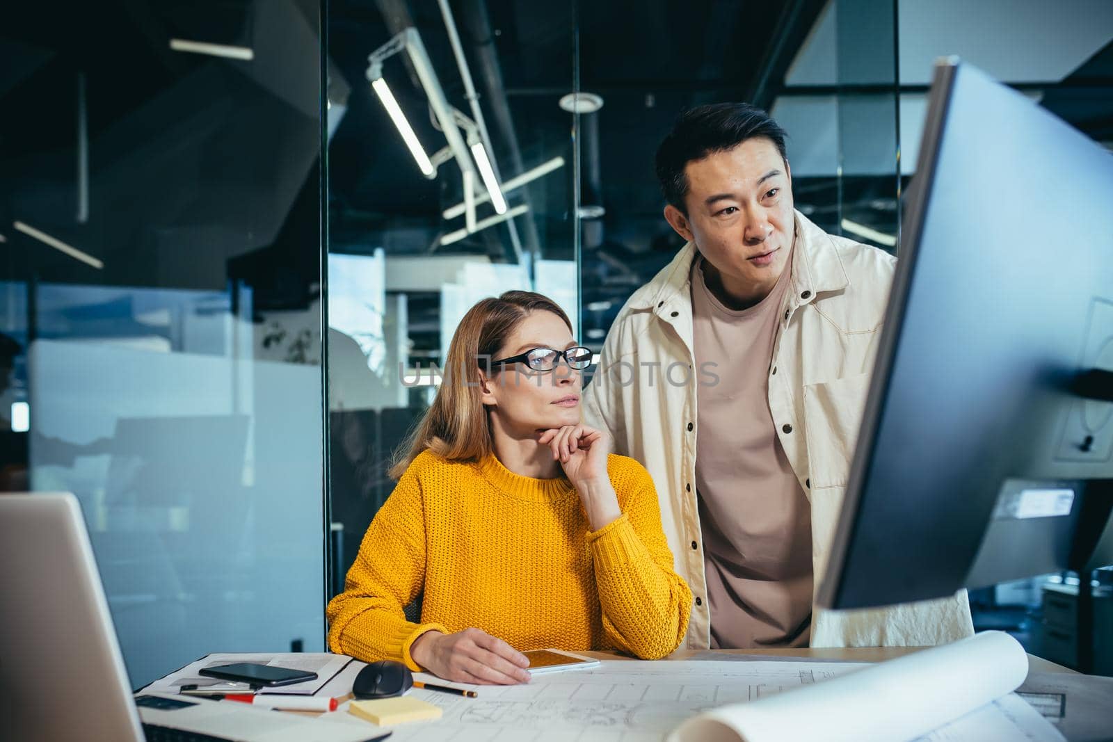 Two freelancers, an Asian man and a woman, work in a modern office by voronaman