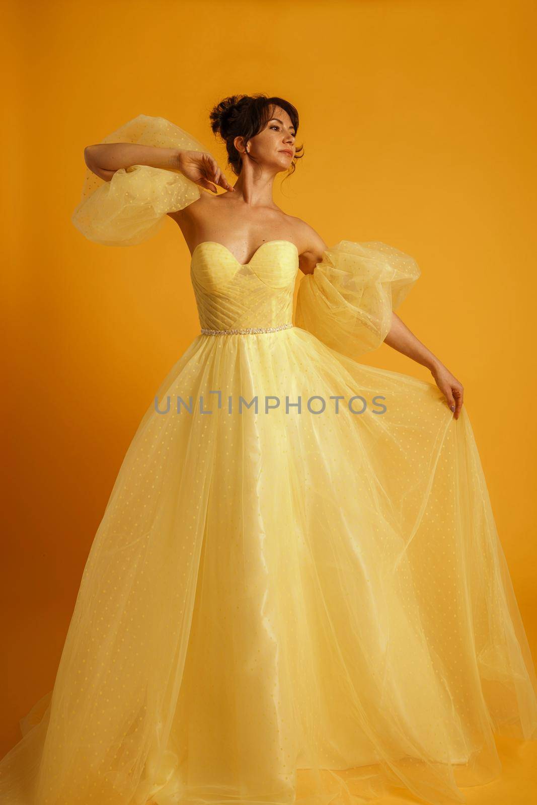 Portrait of a beautiful middle-aged woman in a yellow dress, her hair pulled up against a yellow background by Matiunina