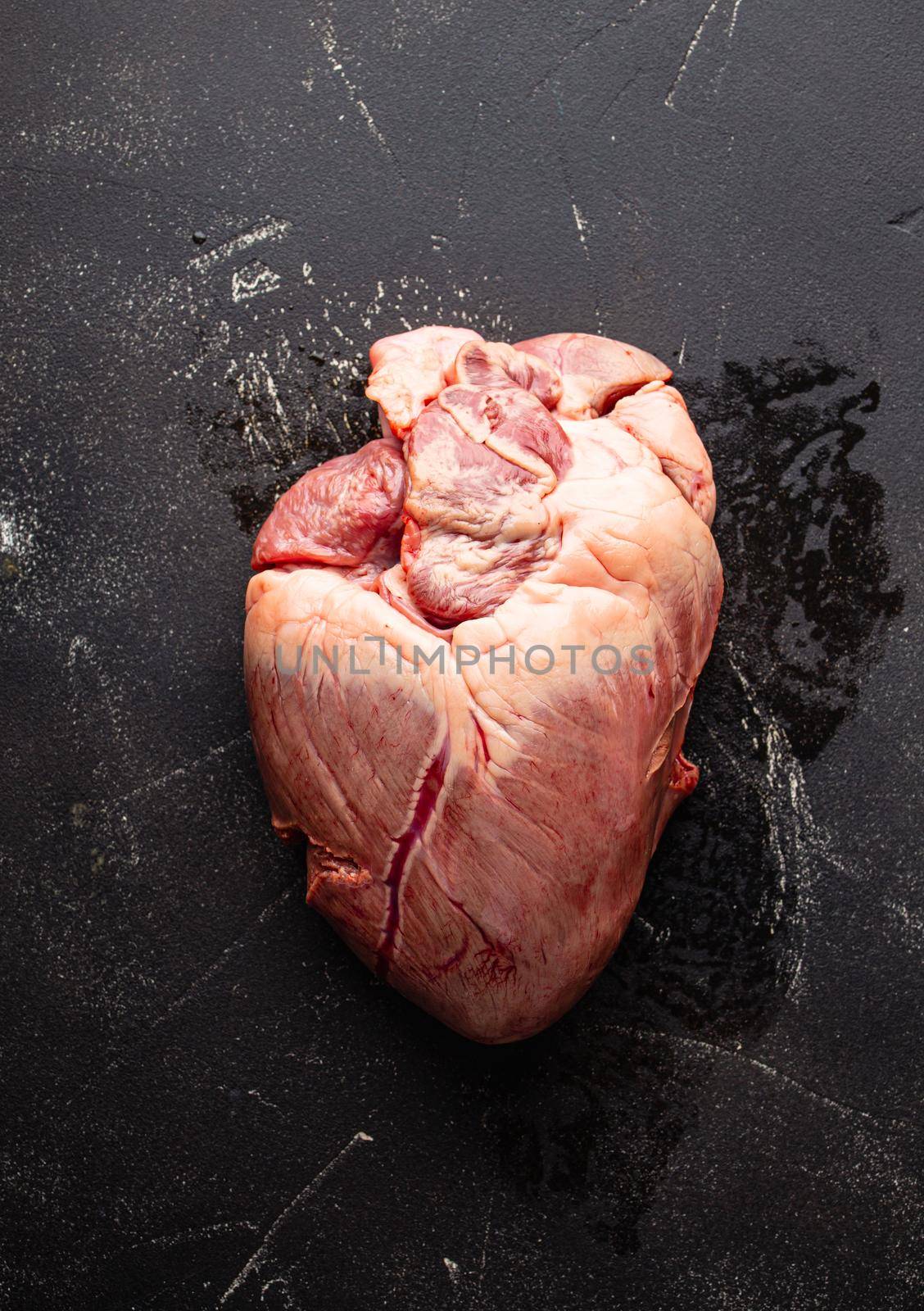 Raw uncooked whole beef or pork heart on black rustic stone background from above, offal and variety meats