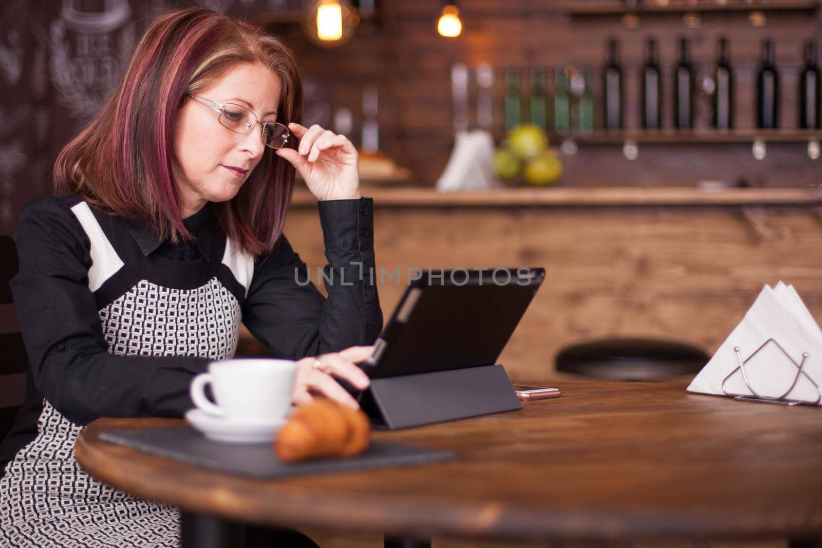 Businesswoman holding her glasses while looking at tablet. Adult antrepreneur woking on vintage coffee shop