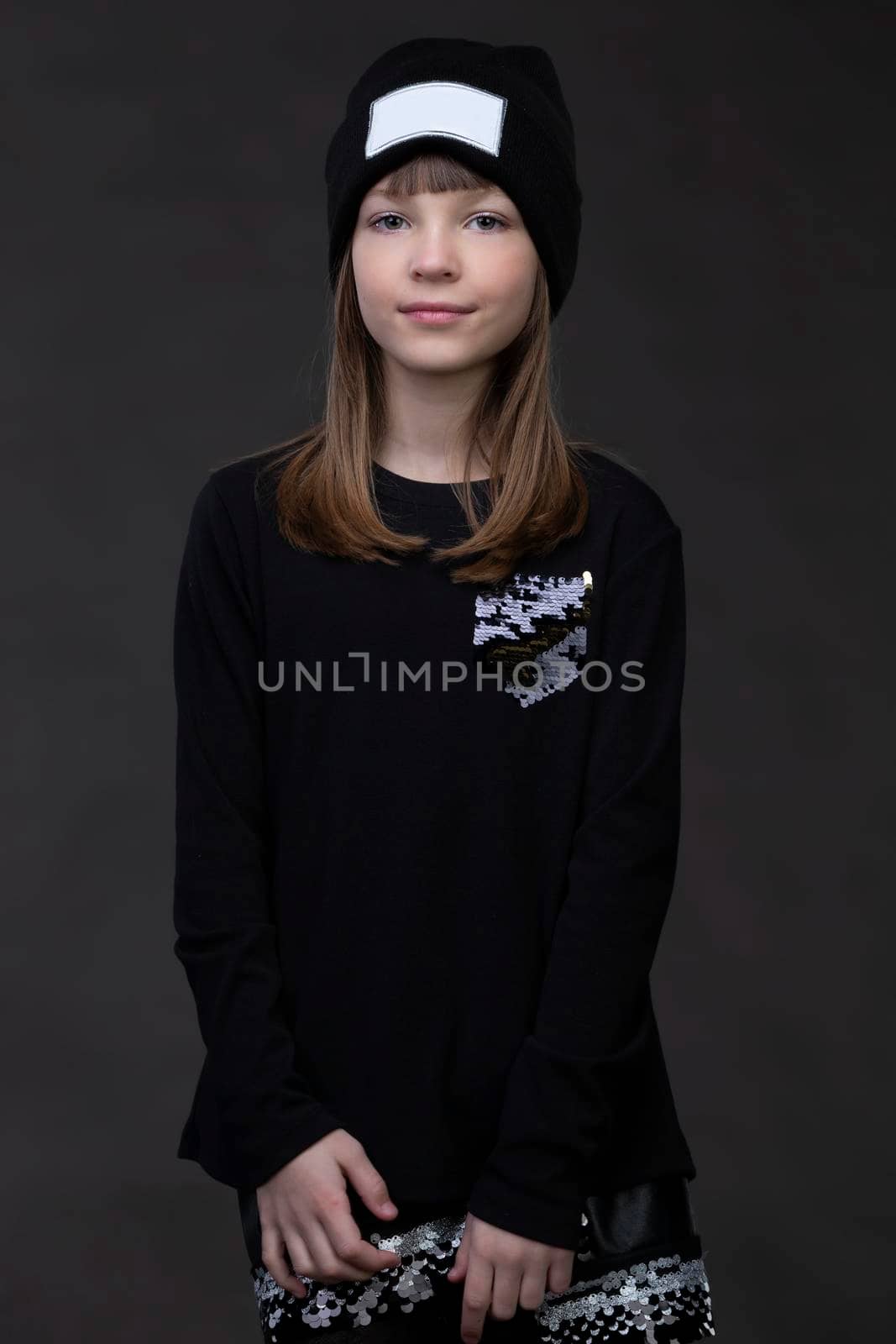 Teenage girl in dark clothes on a gray background posing at the camera.