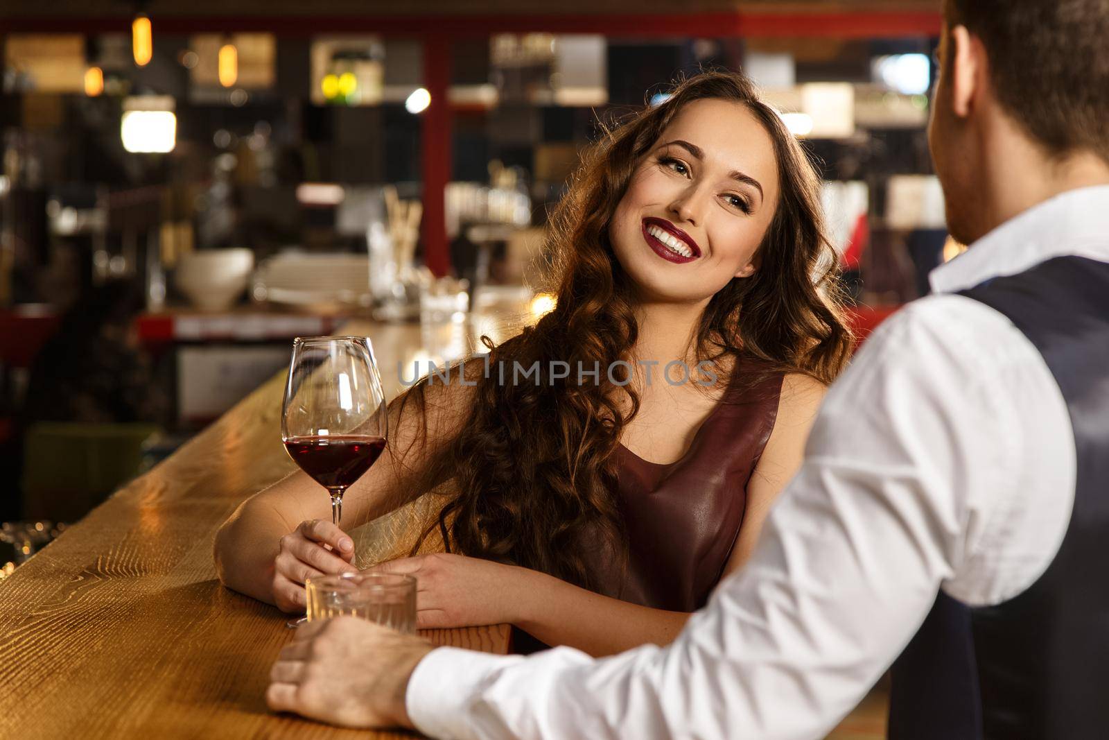 Smile speaks more than words. Beautiful young woman holding a glass of wine smiling joyfully to her man on a date at the bar