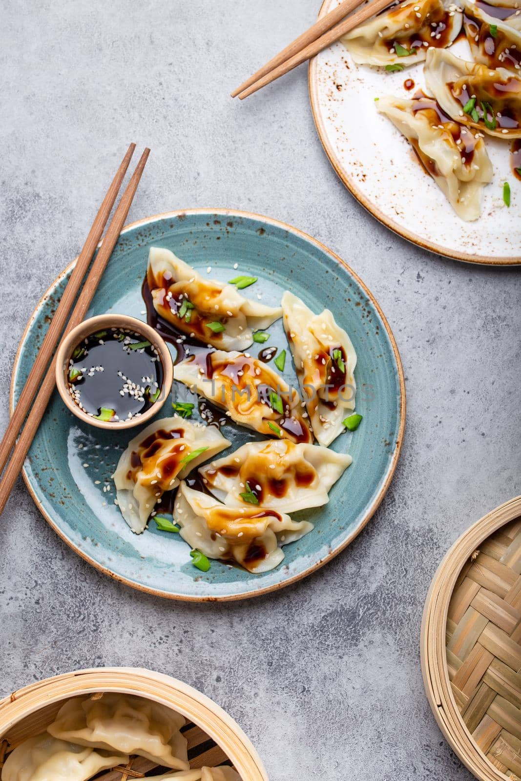 Close-up, top view of two plates with traditional Asian dumplings with soy sauce and chopsticks on gray rustic stone background. Authentic Chinese cuisine