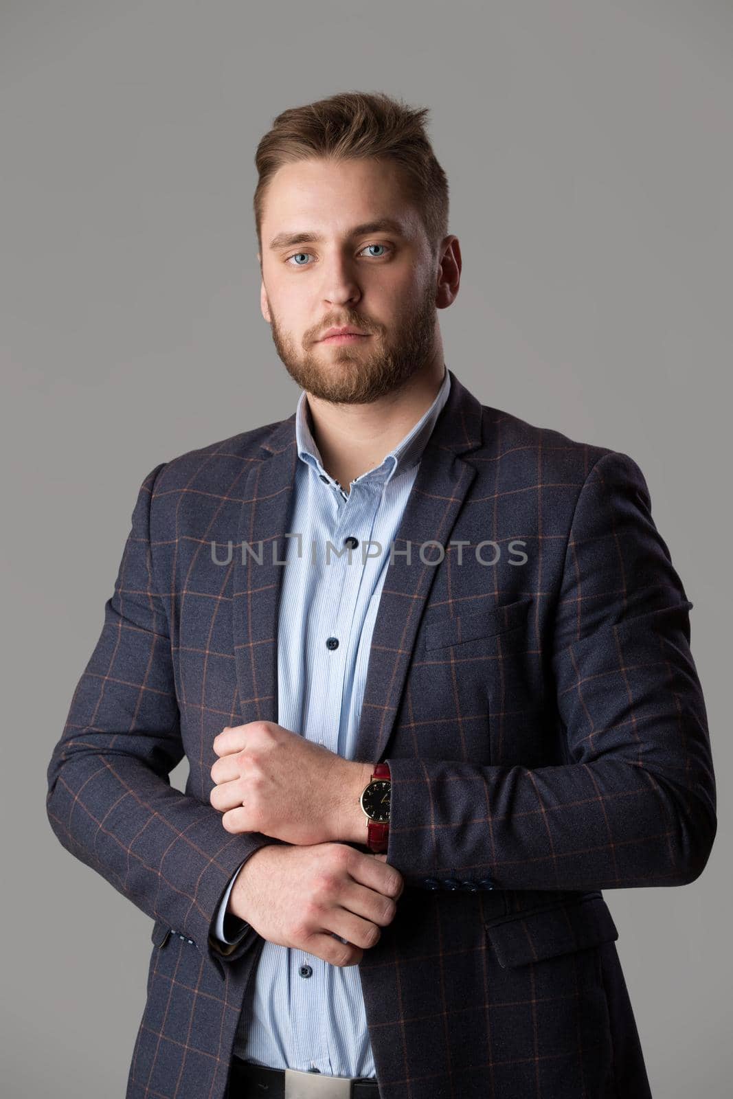A handsome bearded man in a jacket and shirt on a gray background looks at the camera. by Sviatlana