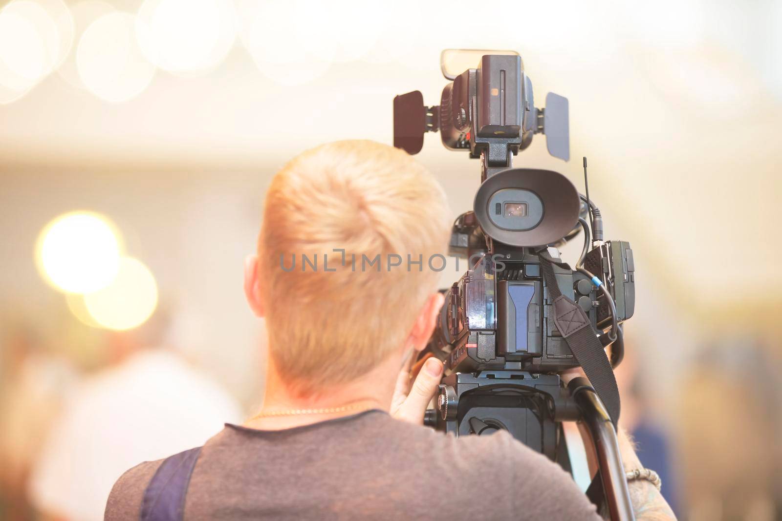 A videographer with a camera stands with his back.