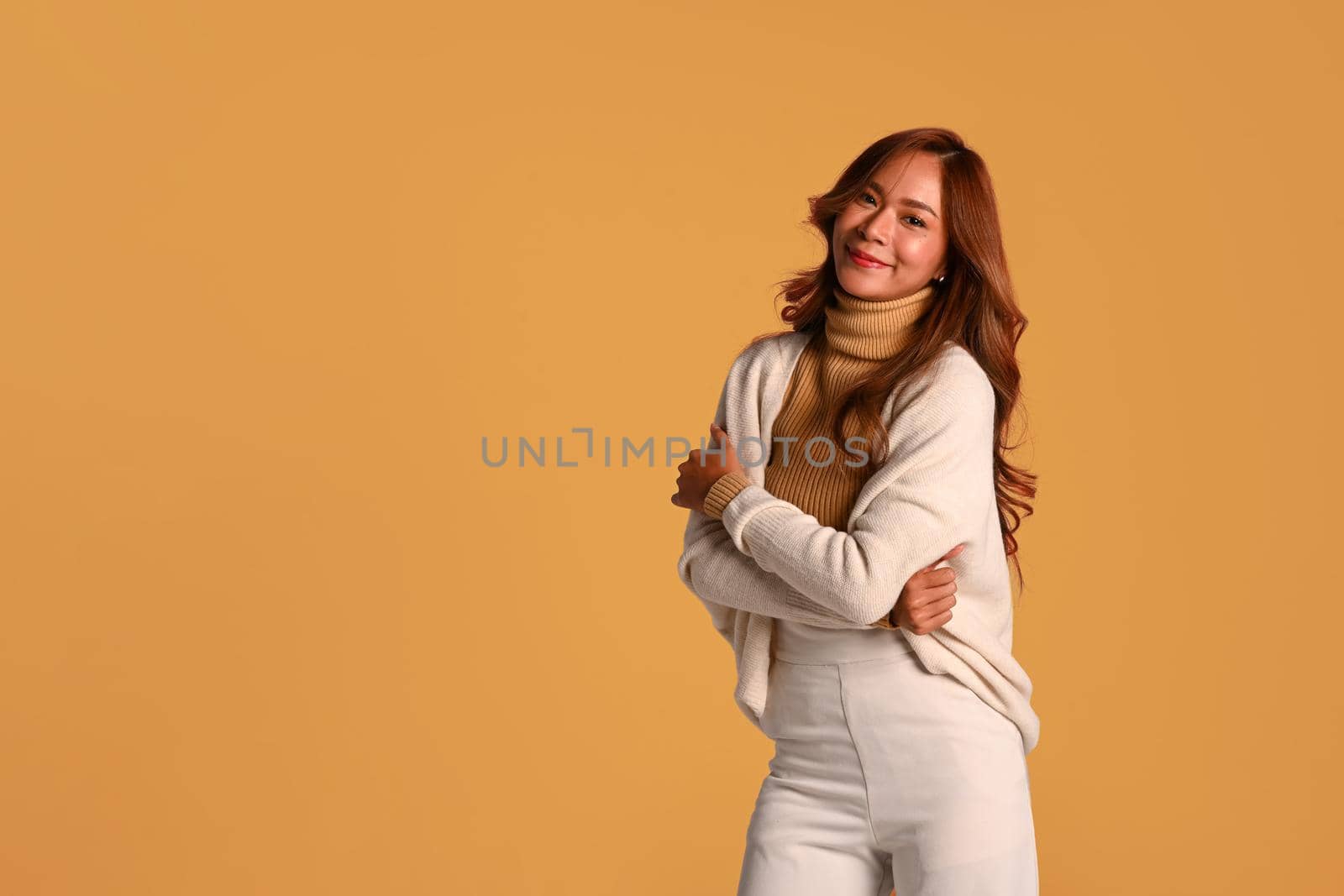 Fashion studio photo of attractive woman in trendy sweater standing over yellow background. Autumn and Winter concept by prathanchorruangsak