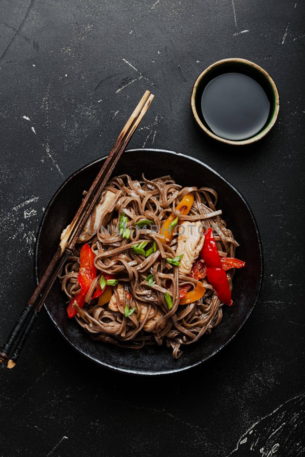 Bowl with Asian chicken stir fry soba noodles with vegetables on dark black stone background from above, Chinese Thai or Japanese noodles dish with soy sauce