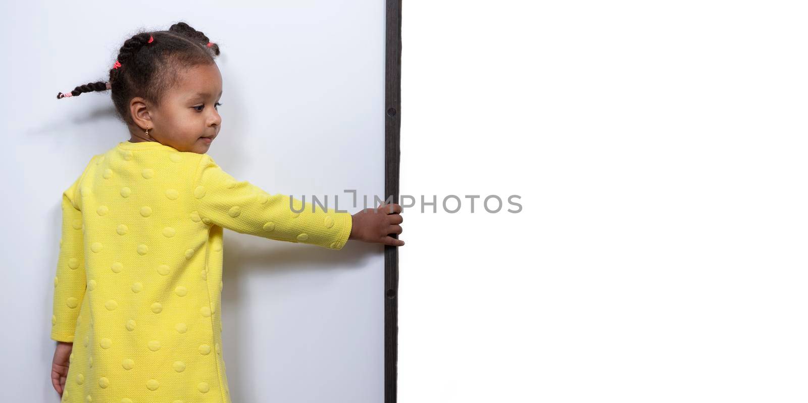 Little African American girl in a yellow dress holds with her hand a blank white sheet for an inscription.