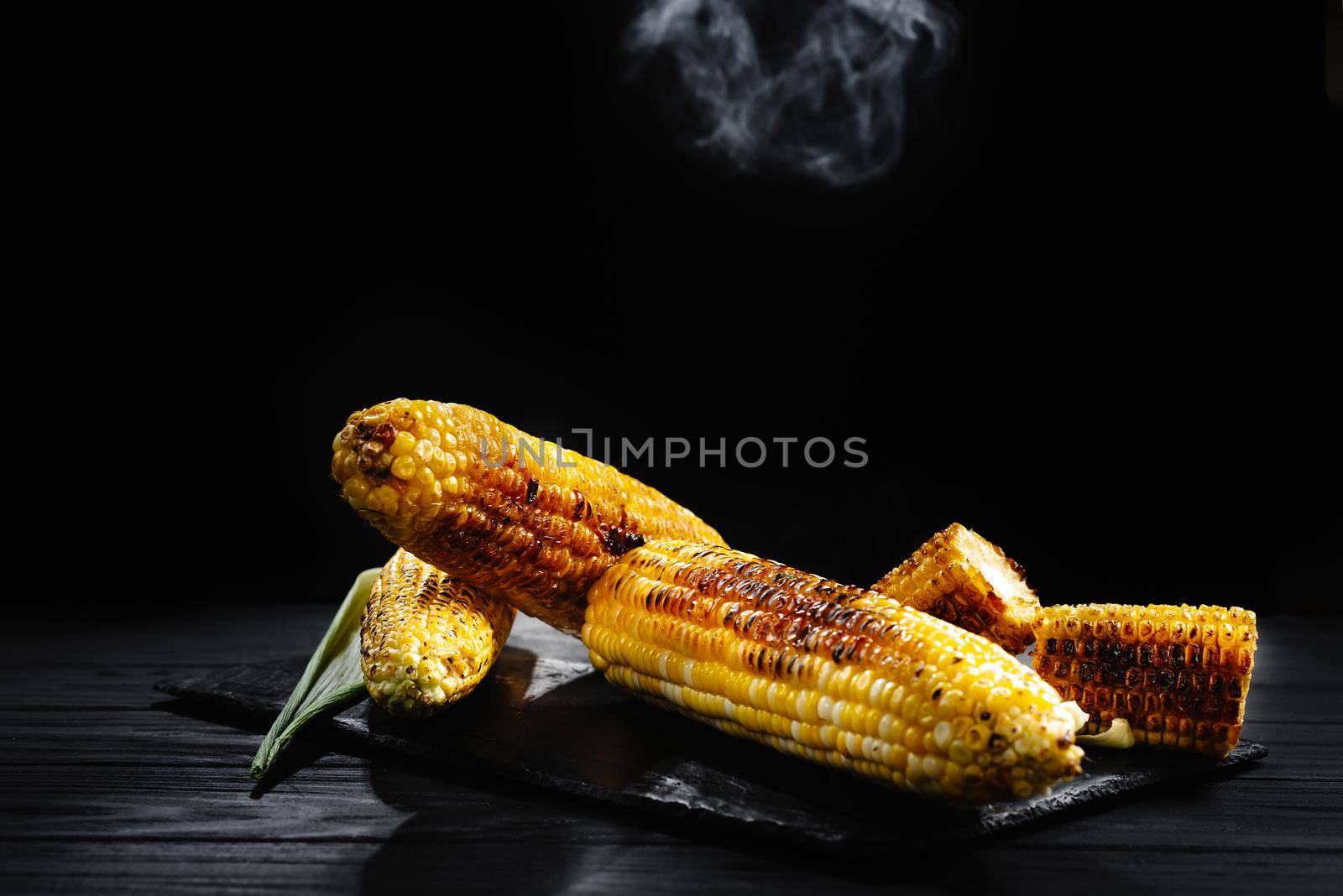 Grilled corn with smoke. A cob of corn roasted over charcoal on a wooden board. Whole corn cobs. by gulyaevstudio
