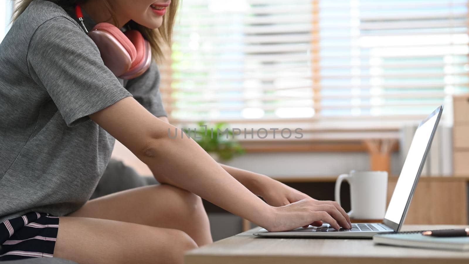Cropped view of woman in casual clothes sitting on couch and using laptop, spending time on weekend by prathanchorruangsak