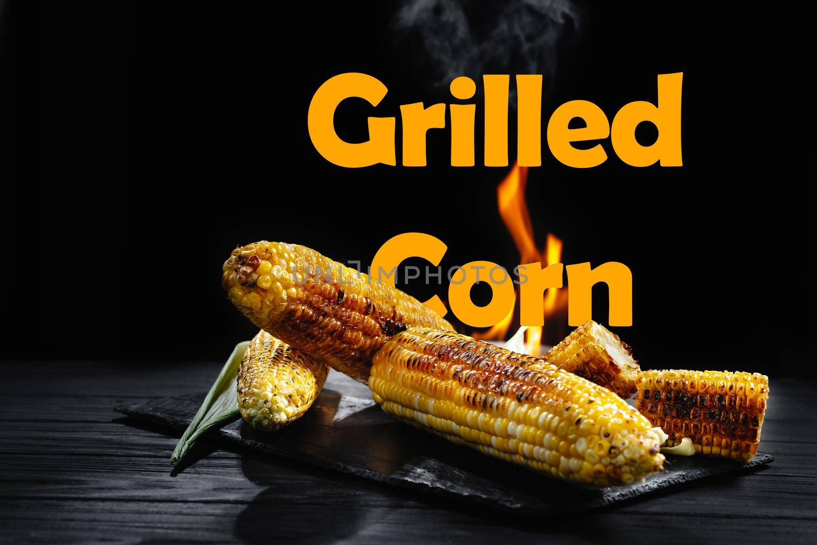 Corn cob on the grill with smoke and flames against a black backdrop. Grilled corn inscription by gulyaevstudio