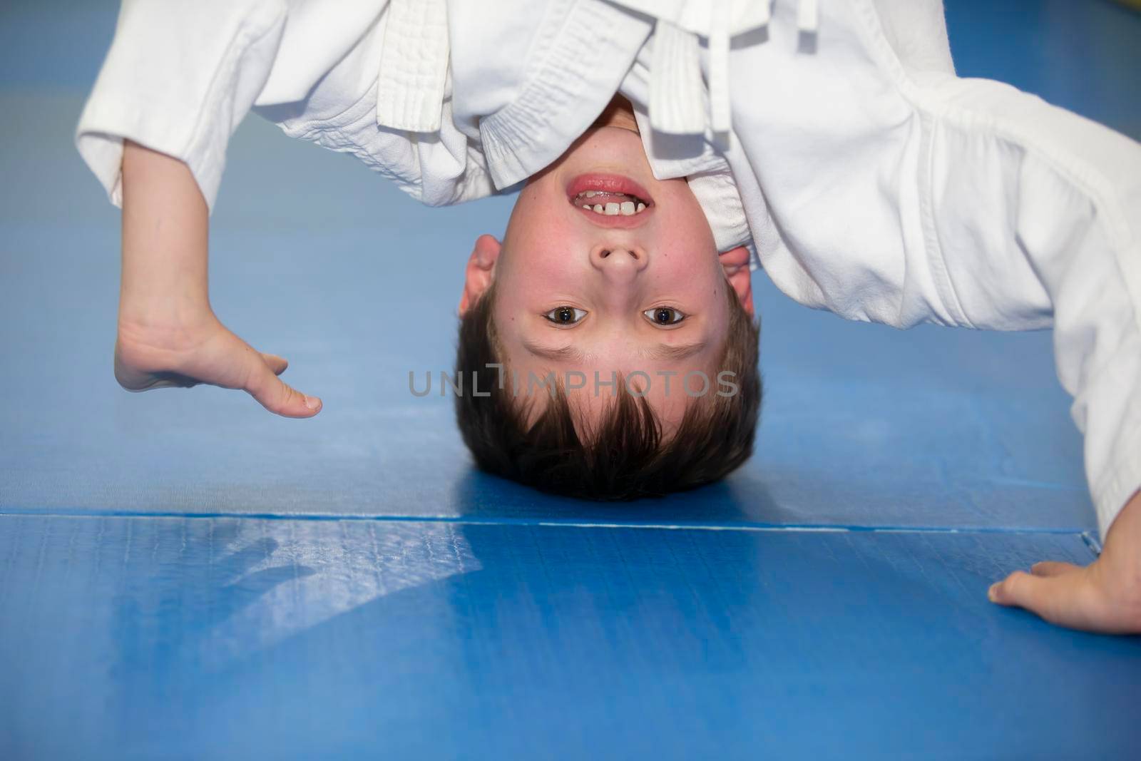 A small boy in a kimano upside down. The child is engaged in judo or karate. Section for children of combat sports.