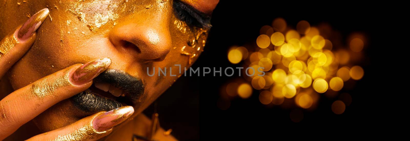 Beauty fashion model girl with golden make-up and body on black background. Golden body art. The golden face of a beautiful lady is touching. Artistic portrait. by Sviatlana