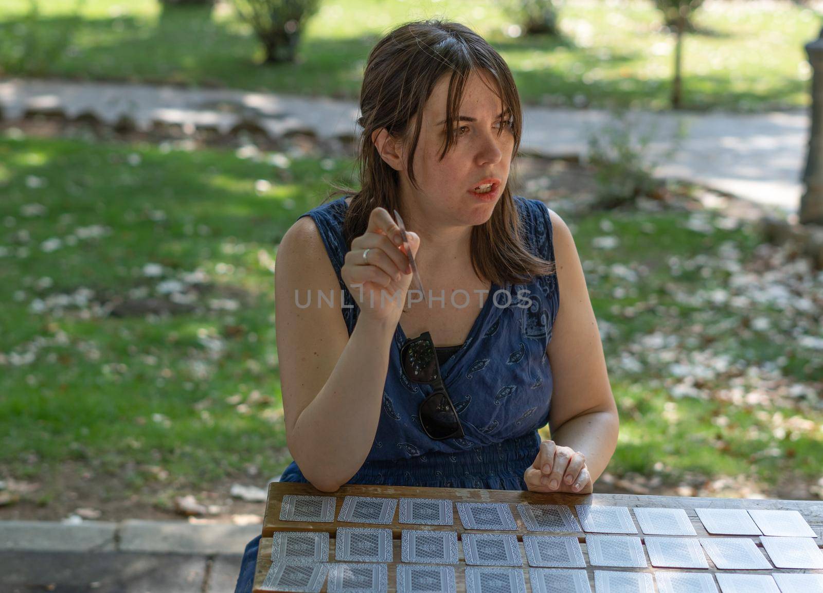 young woman playing cards in the park on a sunny day wearing a blue dress