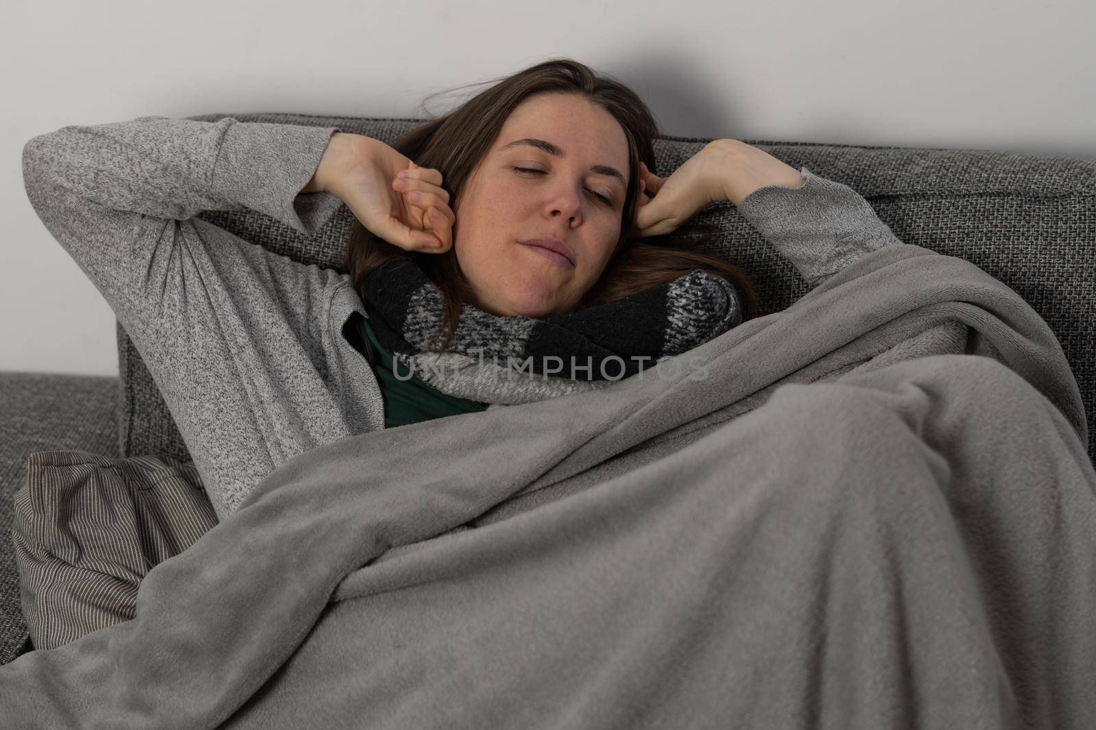 young brunette girl with long hair, sick lying on the sofa in her house taking medicine and an infusion
