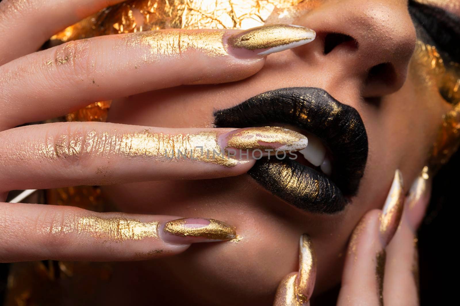 Beauty fashion model girl with golden make-up and body on black background. Golden body art. The golden face of a beautiful lady is touching. Artistic portrait.