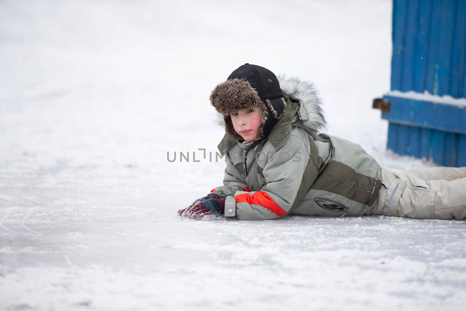 A little boy in a fur hat lies on the snow. Child in winter.
