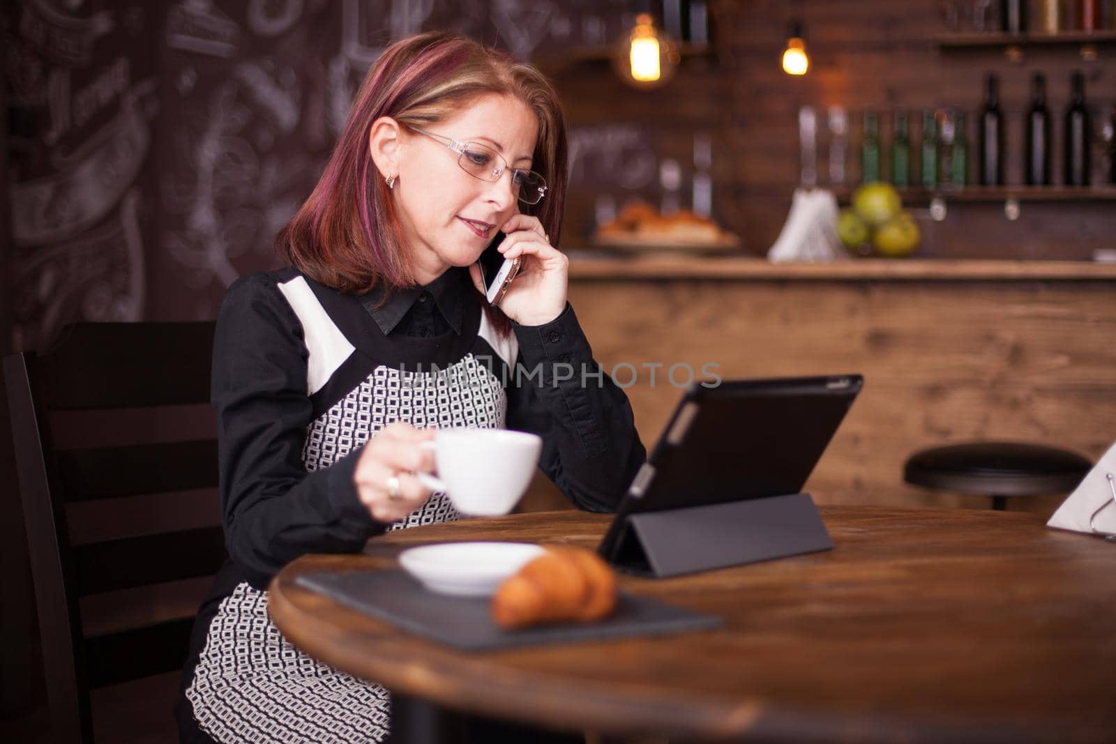 Successful adult businesswoman talking on her phone while holding a cup of coffee. Vintage restaurant