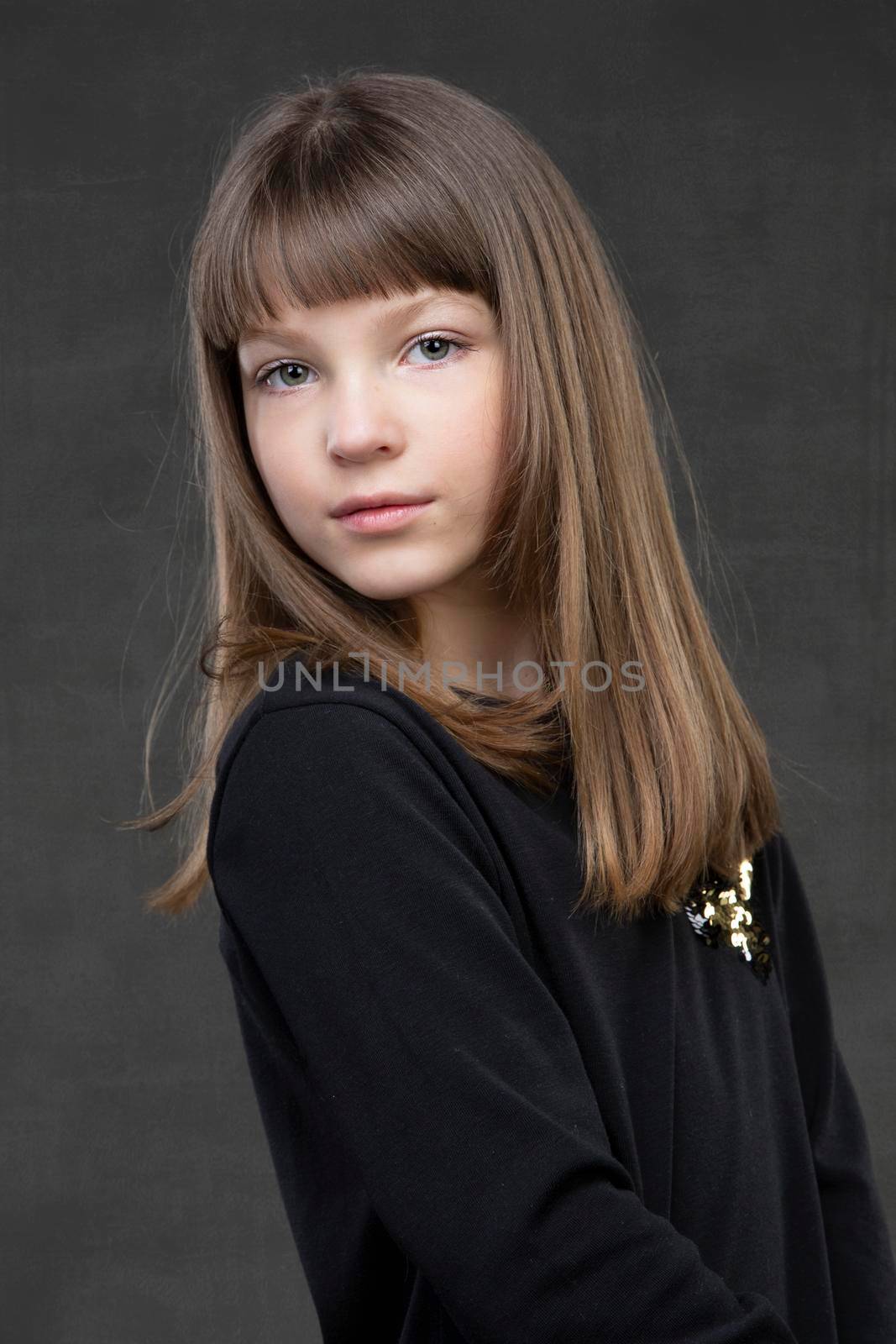 Beautiful little girl look at the camera on a gray background. A child of the European type.