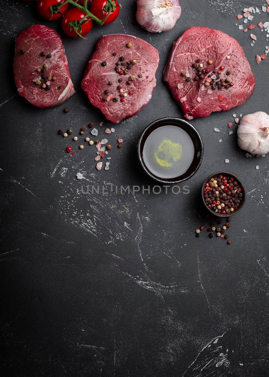 Close-up of raw fresh marbled meat steak on dark rustic concrete background with salt and pepper, olive oil, garlic ready ti be cooked. Cooking meat concept with space for text, top view