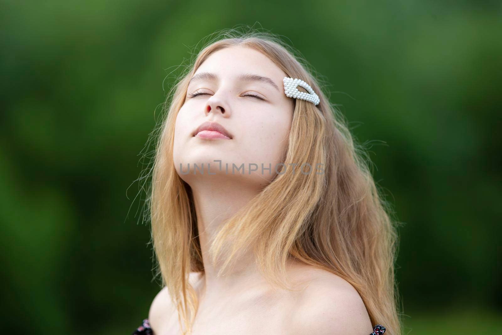 A beautiful girl with long hair closed her eyes on a summer background. The face of a fair-haired teenage girl.