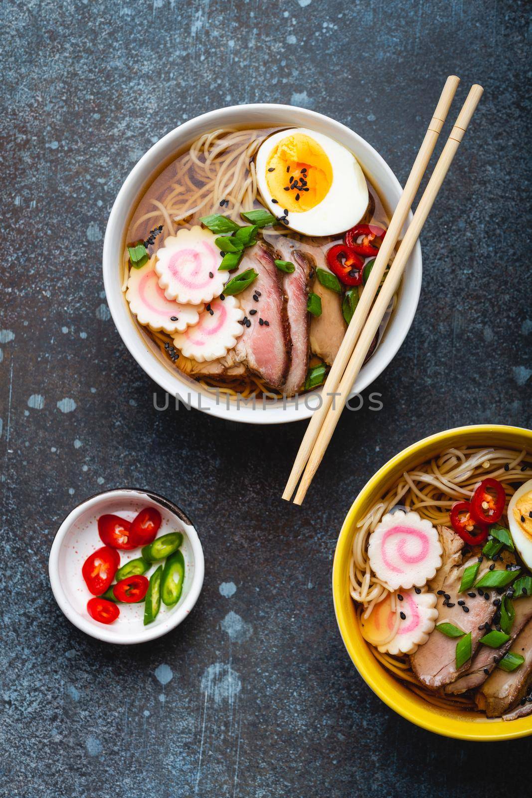 Two bowls of Japanese noodle soup ramen with meat broth, sliced pork, narutomaki, egg with yolk on rustic stone background. Traditional dish of Japan, top view, close-up, concept