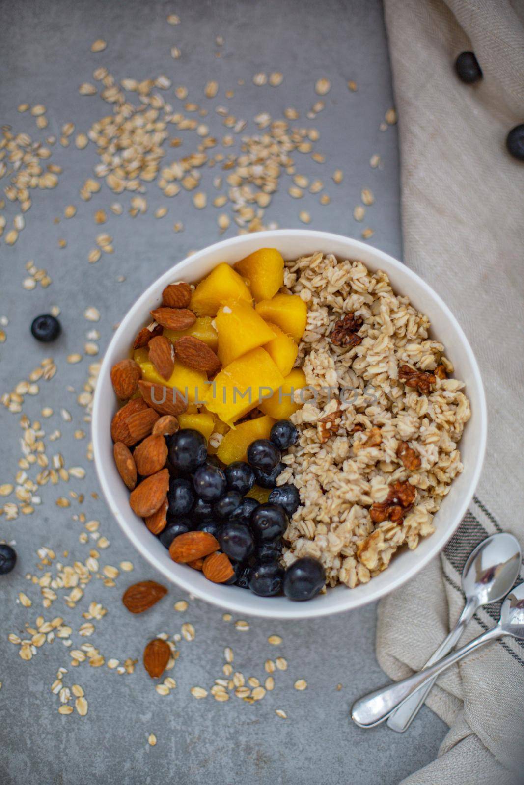 Oatmeal porridge with blueberries, mango and almonds in bowl on concrete grey table from above. flatlay. Healthy breakfast food. Copy space