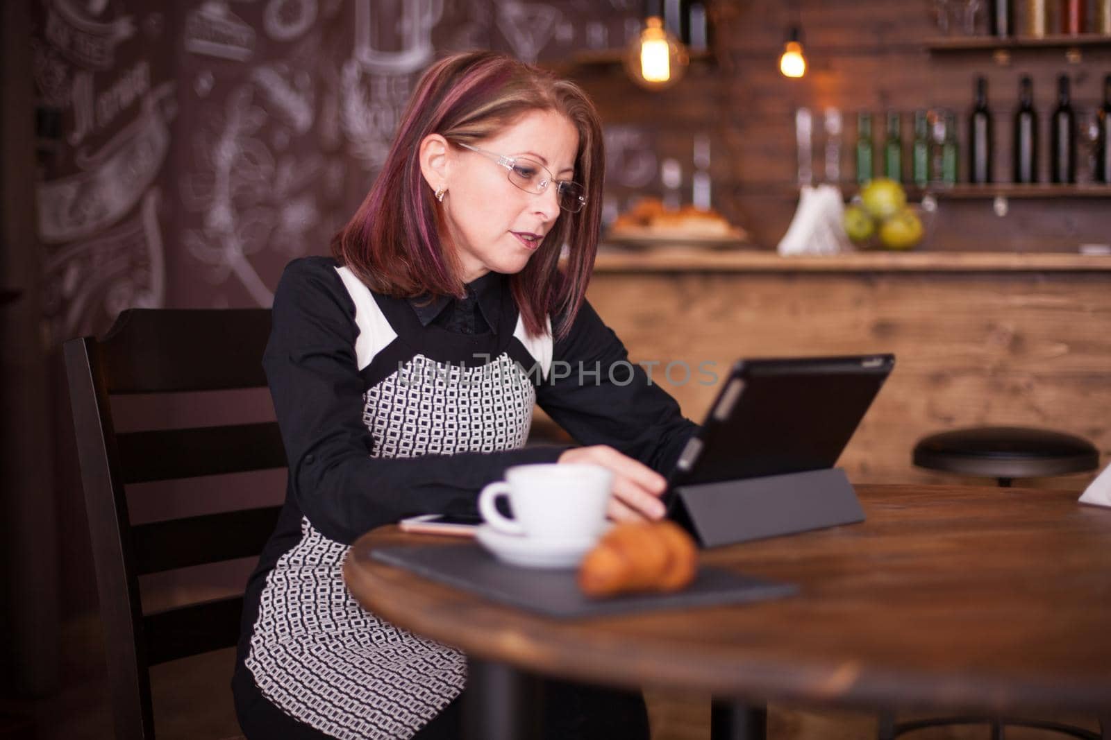 Beautiful smiling adult woman enjoying coffe while working on her tablet by DCStudio