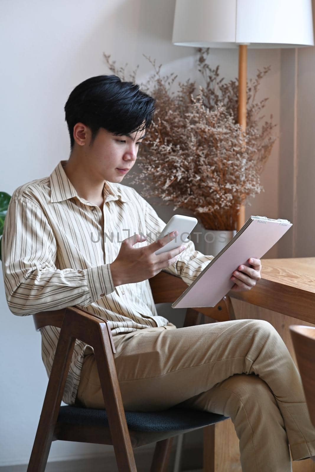 Handsome Asian man holding smart phone and using digital tablet in cafe.